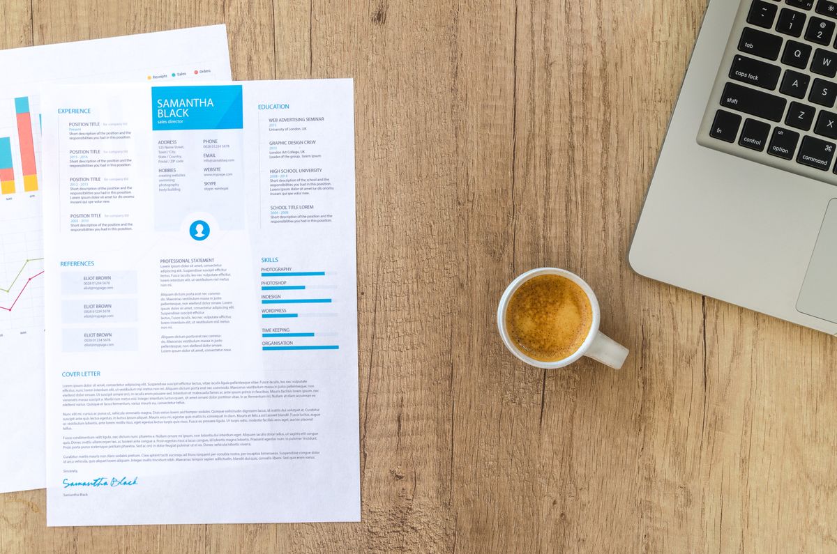 Schreibtisch mit Laptop, Kaffee­tasse, Lebenslauf und bedruckter Seite mit farbigen Diagrammen im hellen Holz